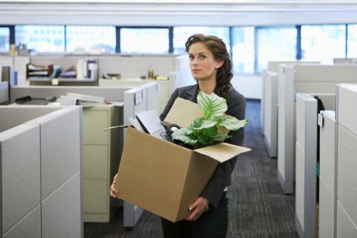 Mujer saliendo de una oficina con una caja de pertenencias tras ser despedida.