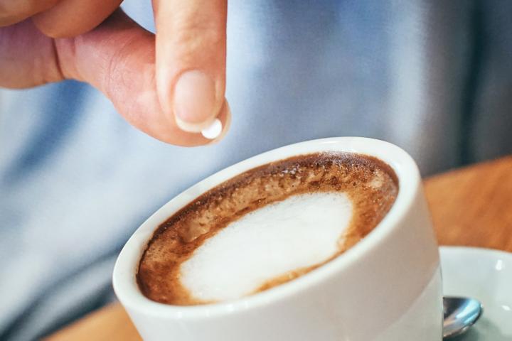 Una persona endulzando un café con aspartamo.