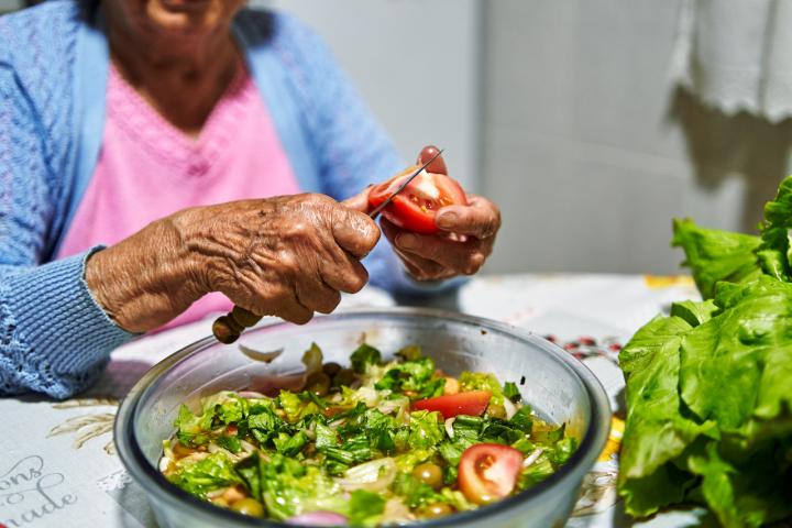 Una mujer corta varios tomates para preparar una ensalada.