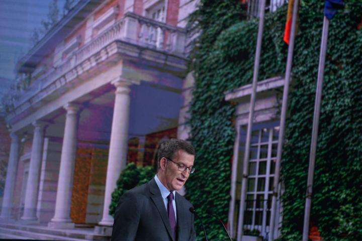 El líder del PP, Alberto Núñez Feijóo, durante la presentación del programa con La Moncloa proyectada de fondo.