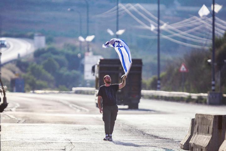Un colono alza una bandera de Israel frente a palestinos en una carretera de Cisjordania