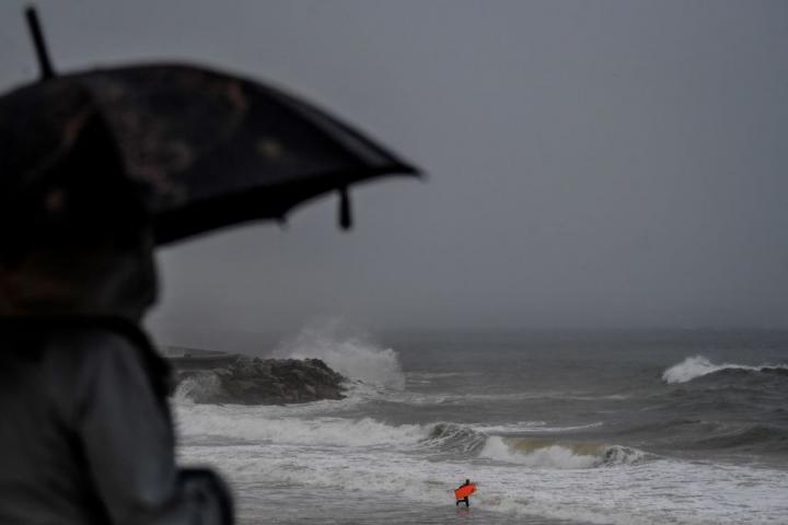 Una persona se cubre bajo un paraguas mientras ve una playa
