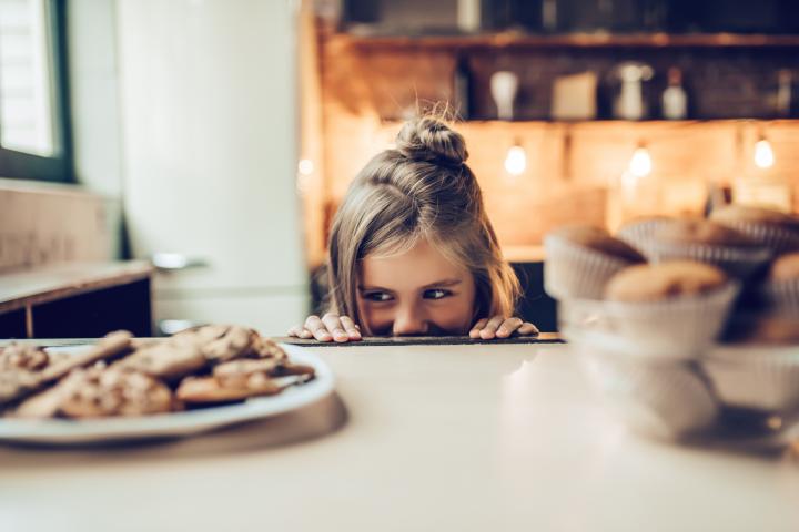 Imagen de archivo de una pequeña observando con interés un plato de galletas.