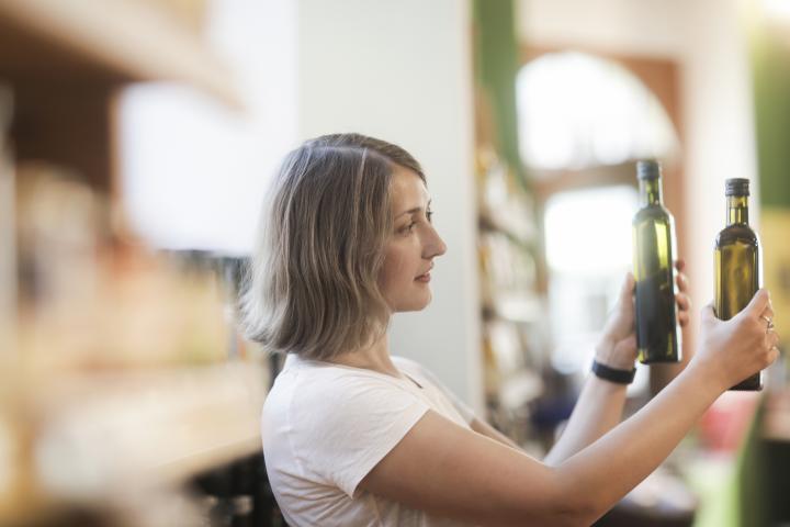 Imagen de archivo de una mujer comparando dos botellas de aceite de oliva en un supermercado.