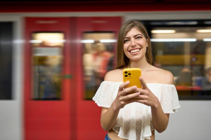 Imagen de archivo de una mujer leyendo algo en su móvil y riéndose, ante un vagón de Rodalies.