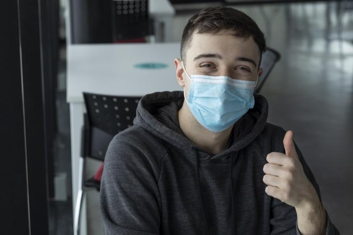 Imagen de archivo con un joven con mascarilla haciendo un gesto afirmativo con el pulgar.
