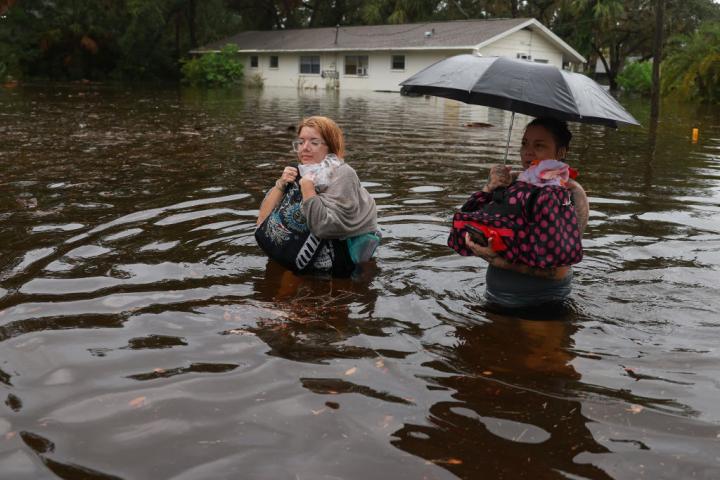 Dos mujeres, con el agua por la cintura, caminan por una ciudad de Floridad tras el paso del huracán Idalia.