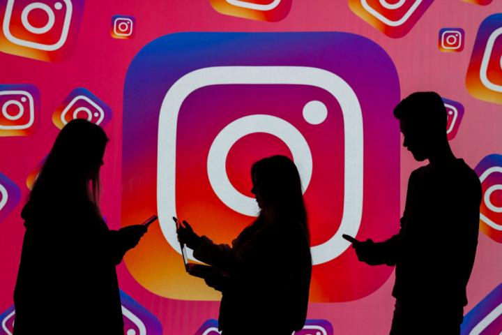 La silueta de varias personas delante de una pantalla con el logotipo de Instagram.