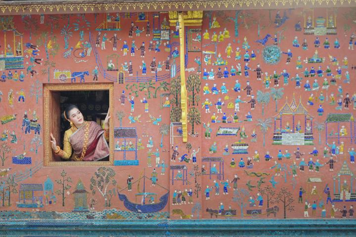 alt="alt="Una mujer asomada por la ventana de un templo en Wat Xieng Thong, Luang Prabang, Laos.""