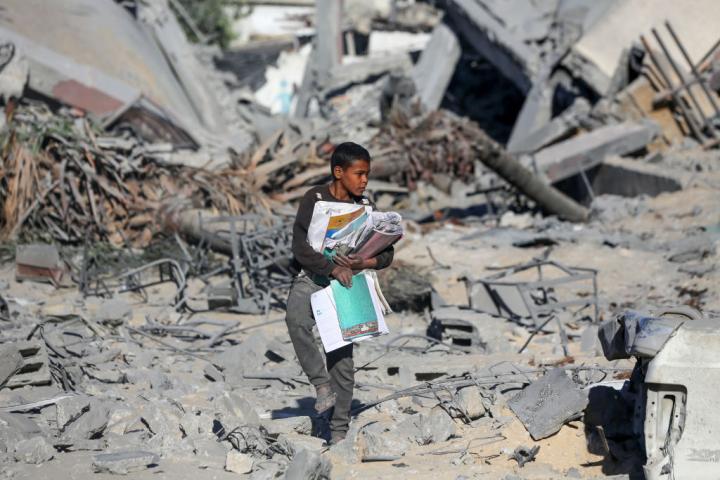 Un menor palestino recoge material escolar entre los escombros de la escuela Al-Urube, atacada por Israel en el campamento de Nuseirat.