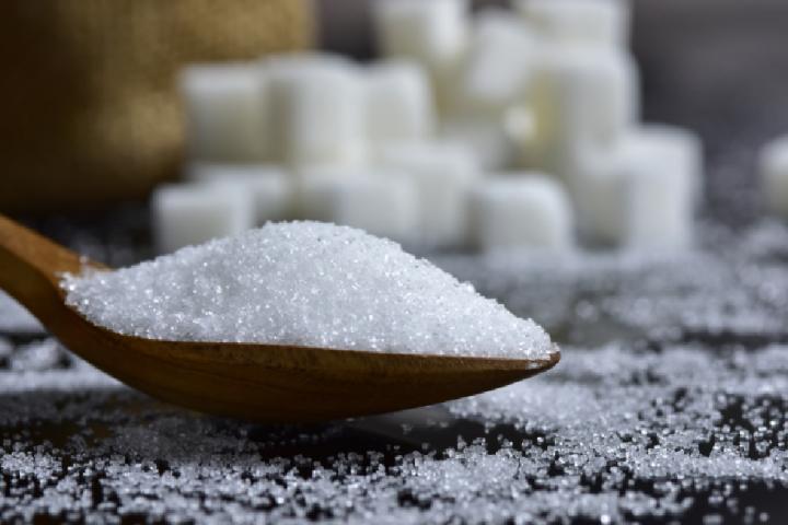 Cucharada de azúcar con terrones de fondo.