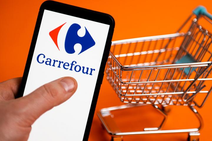 Ilustración del logotipo de Carrefour en la pantalla de un móvil, con un carrito al fondo.