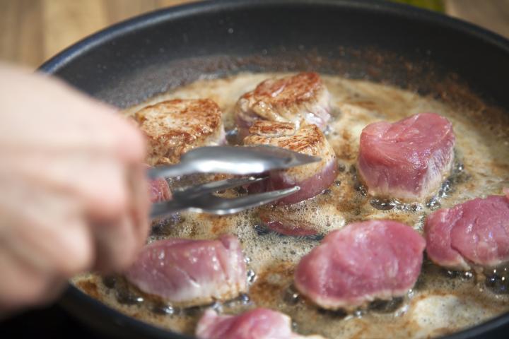 Un cocinero con carne en la sartén.