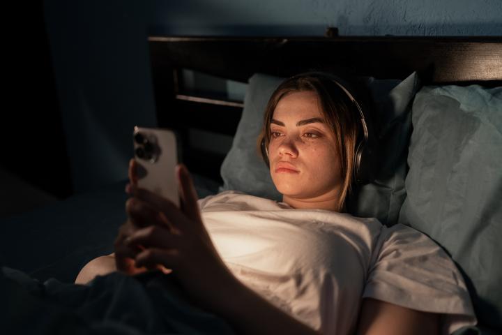Imagen de archivo de una mujer joven en la cama con un móvil.