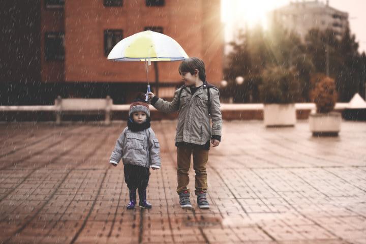 Imagen de archivo de un niño cubriendo a otro con un paraguas.