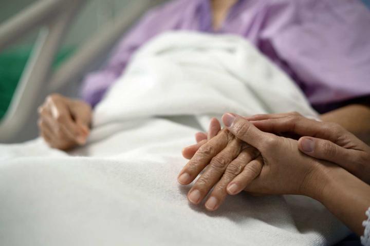 Una hija le sostiene la mano a su madre en el hospital