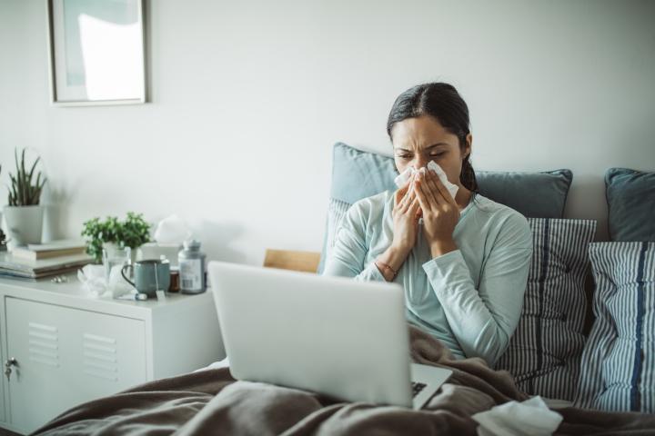 Una mujer con gripe, en cama con el ordenador del trabajo.