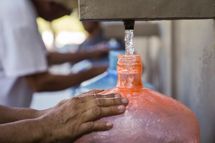Una persona llenando un recipiente con agua.