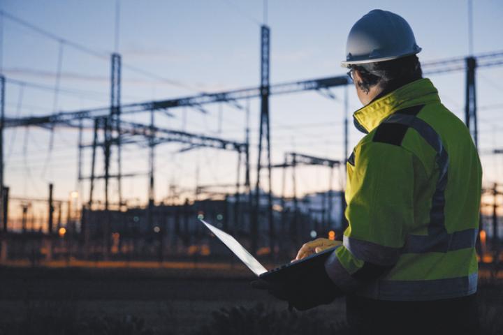 Un ingeniero comprueba su portátil con una planta eléctrica al fondo.
