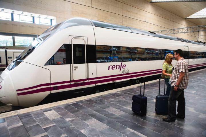 Dos personas pasan con su maletas por delante de un tren de Renfe, en Zaragoza.