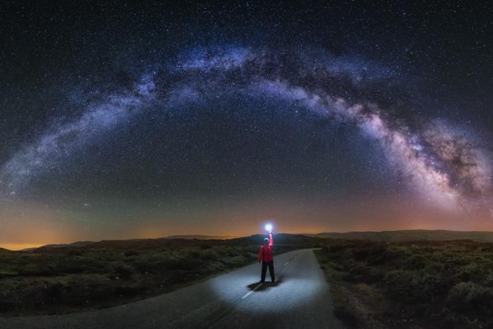 Un joven observa la Vía Láctea en A Veiga, Ourense, y alumbra el camino con una linterna.