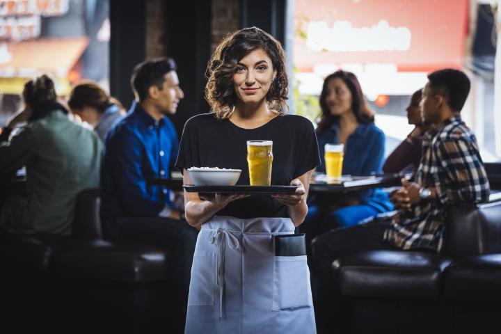 Imagen de archivo de una camarera llevando una caña de cerveza a una mesa.