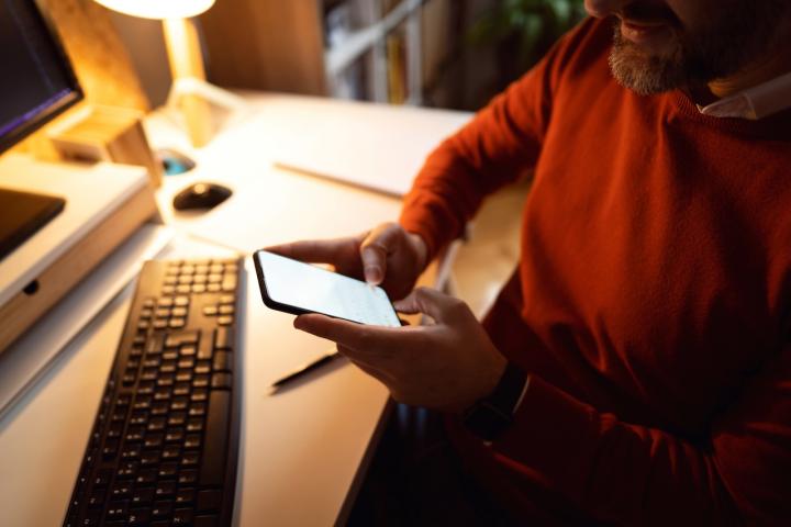 Un hombre cisgénero heterosexual caucásico utiliza su teléfono móvil mientras trabaja desde casa.