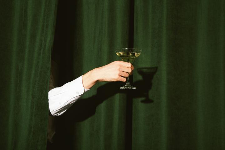 Imagen de archivo de una mano sujetando un 'dry martini' (martini seco) con un telón verde de fondo.