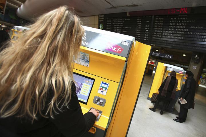 Una joven compra un billete de tren en una estación de París.
