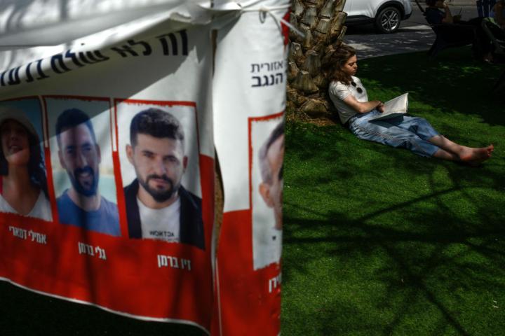 Una joven lee en una zona verde de Tel Aviv cerca de un cartel con las caras y nombres de los secuestrados por Hamás.