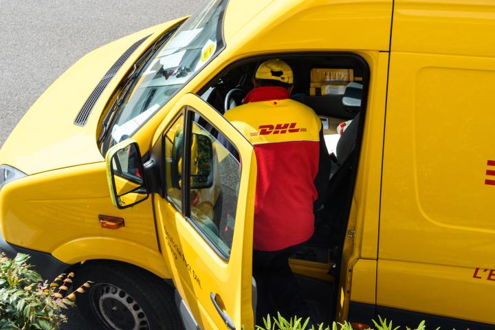 El mensajero ingresa a la furgoneta de entrega amarilla de DHL después de entregar el paquete