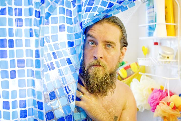 Un hombre se asoma por las cortinas de la ducha.