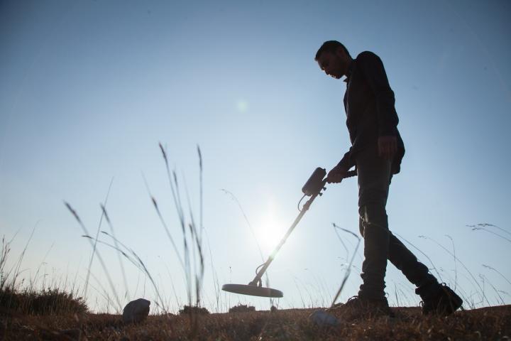 Un hombre busca los restos de un tesoro valiéndose de un detector de metales.