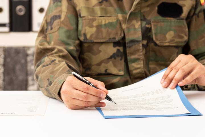 Imagen de una persona vestida con uniforme militar, firmando un documento.