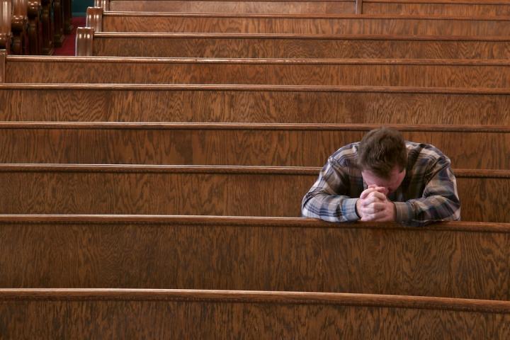 Un hombre, de rodillas, reza en una iglesia.