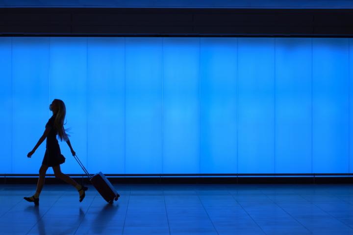 Imagen de la silueta de una mujer, andando en un aeropuerto con una maleta.