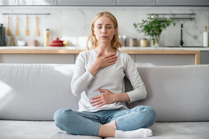 Mujer sentada en un sofá haciendo ejercicios de respiración para calmarse después de un ataque de ansiedad.