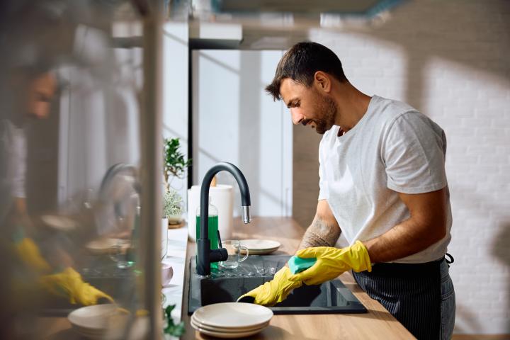 Un hombre fregando los cacharros y recogiendo la cocina.