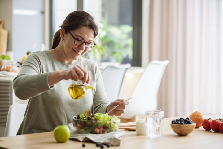 Una mujer echando aceite de oliva a su ensalada.