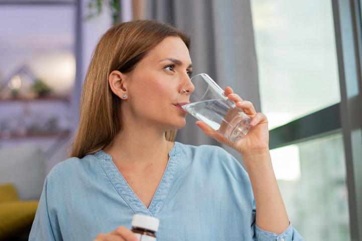 Una chica tomando un baso de agua con un bote en la otra mano