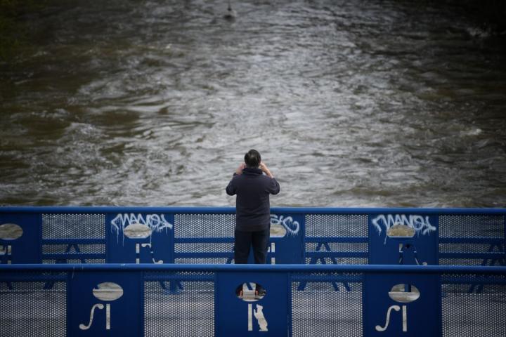 Una persona fotografía el curso del río de Manzanares, crecido por las intensas lluvia que trae la borrasca Martinho.