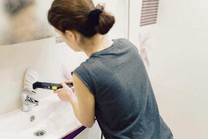 Una mujer limpiando los azulejos del baño con un cepillo eléctrico.