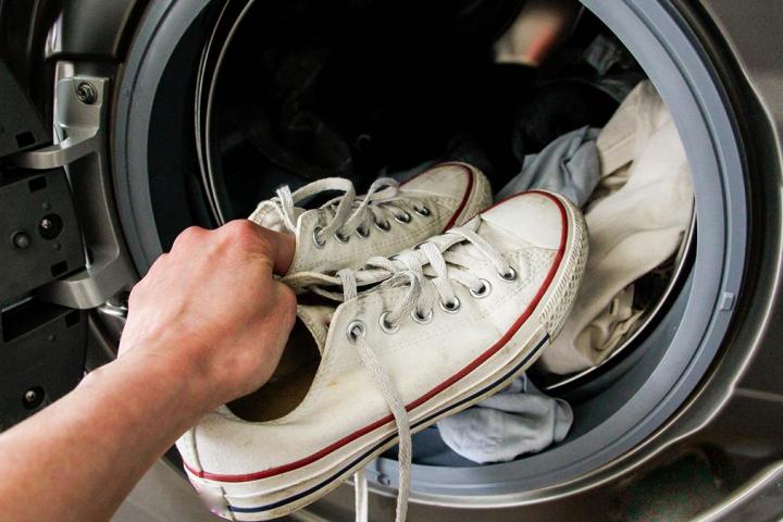 Un mano metiendo unas zapatillas en la lavadora
