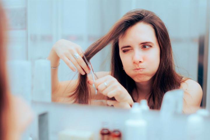 una chica con una tijeras a punto de cortarse un mechón de pelo con unas tijeras.