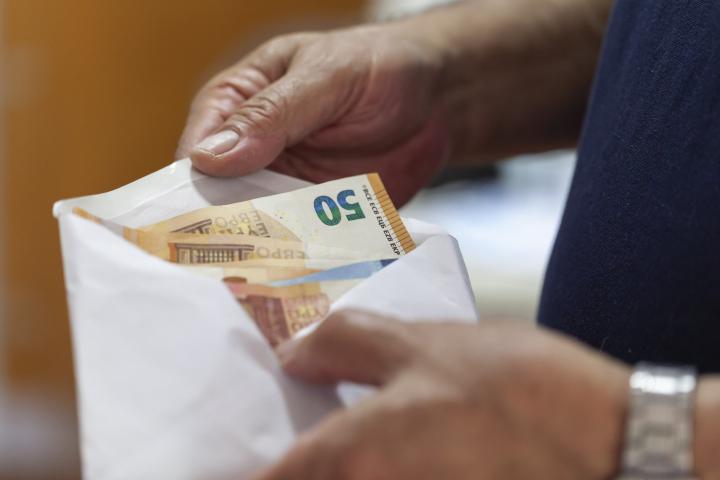 “Manos de una persona mayor sosteniendo un sobre con billetes de euro, relacionado con el timo del tocomocho en Burgos”