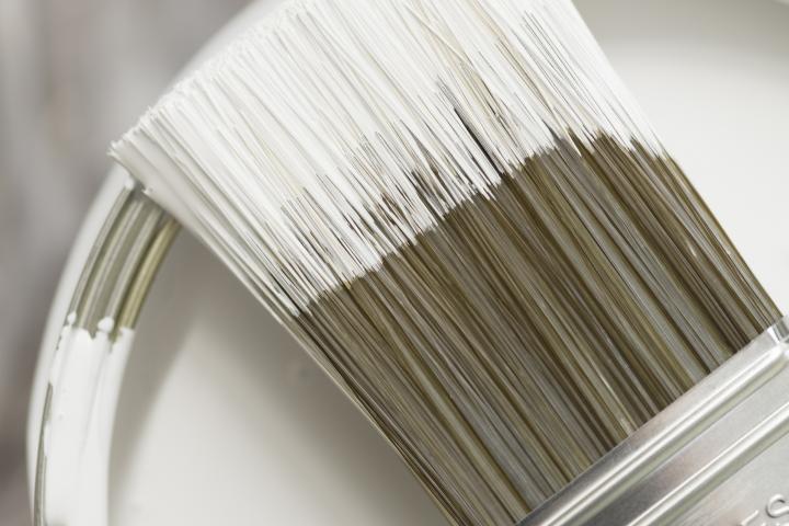 Imagen de archivo de un cubo de pintura blanca y una brocha.