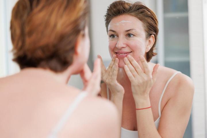 Una mujer echándose crema frente al espejo