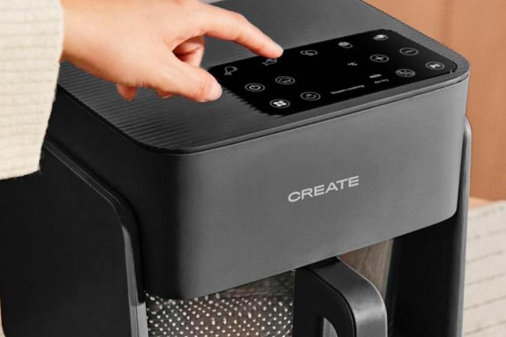 Una freidora con cesta de cristal siendo encendida por una mano.