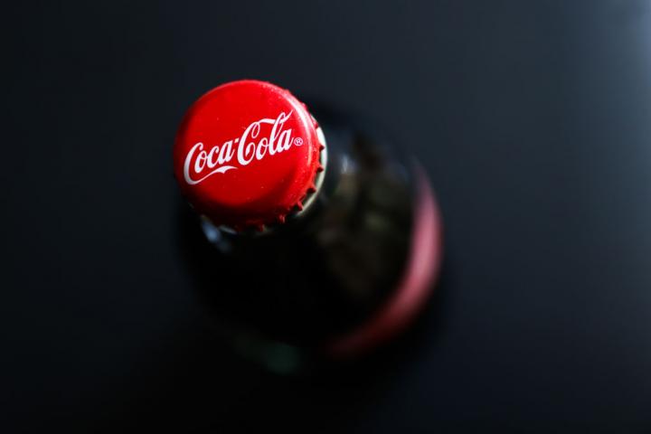 Primer plano del tapón rojo de una botella de Coca-Cola sobre fondo negro.