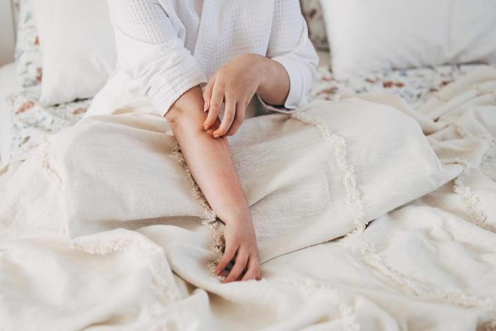 Una persona rascándose el brazo en la cama al despertar.